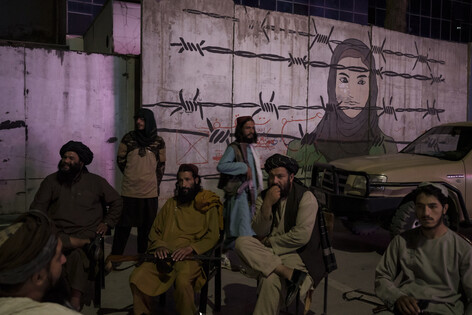 탈레반 대원들이 21일 카불에서 여성의 얼굴이 그려진 벽화 앞에 앉아 있다. 카불/AP 연합뉴스