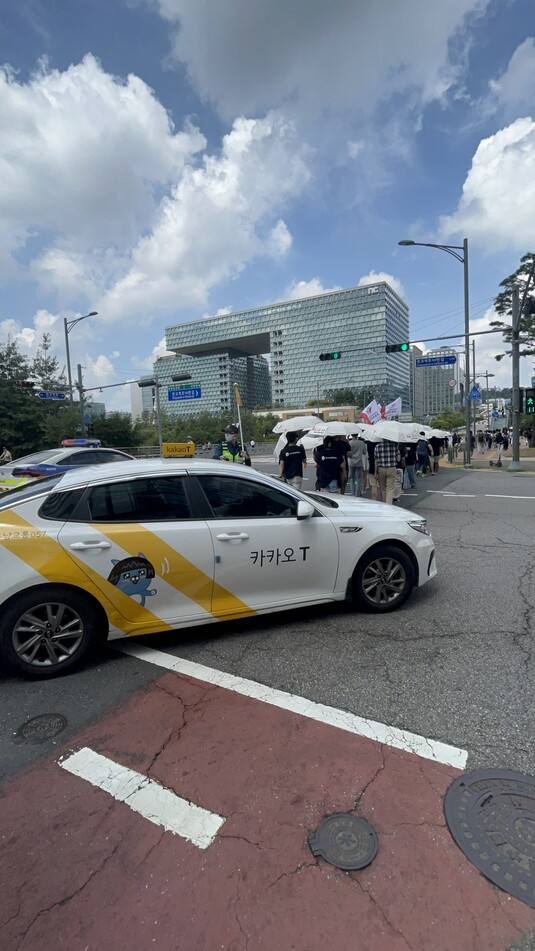 지난 8월17일 카카오 공동체 노동조합이 하얀 우산을 들고 경기도 판교 일대 카카오 계열사 앞을 행진하고 있다. 그 옆을 ‘카카오 티(T) 택시’가 지나고 있다. 임지선 기자