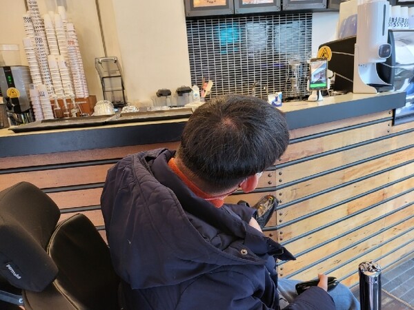 뇌병변장애인 김시형(37)씨가 대구의 한 카페에서 큐아르(QR) 코드를 위해 설치된 휴대전화를 바라보고 있다. 이 휴대전화에는 휠체어를 탄 김씨의 손이 닿지 않는다. 김시형씨 제공