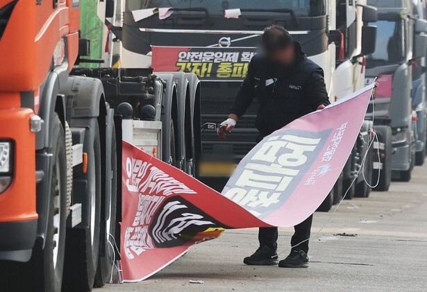 민주노총 전국공공운수사회서비스노조 화물연대본부 파업을 종료하고 현장 복귀를 결정한 9일 오후 경기도 의왕시 내륙컨테이너기지(ICD) 앞에서 관계자가 도로에 세워둔 화물차들에 붙어있던 파업 관련 현수막을 정리하고 있다. 연합뉴스