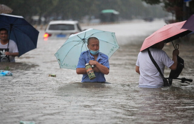 20일 중국 중부 허난성 성도 정저우에서 주민들이 우산을 받쳐 든 채 폭우로 침수된 거리를 지나고 있다. 정저우/로이터 연합뉴스