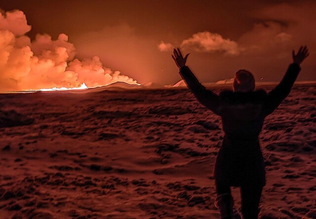 18일(현지시각) 아이슬란드 남서부 레이캬네스 반도 그린다비크에서 발생한 화산 폭발로 밤하늘이 주황색으로 물든 가운데, 지역 주민이 이를 지켜보고 있다. AFP 연합뉴스