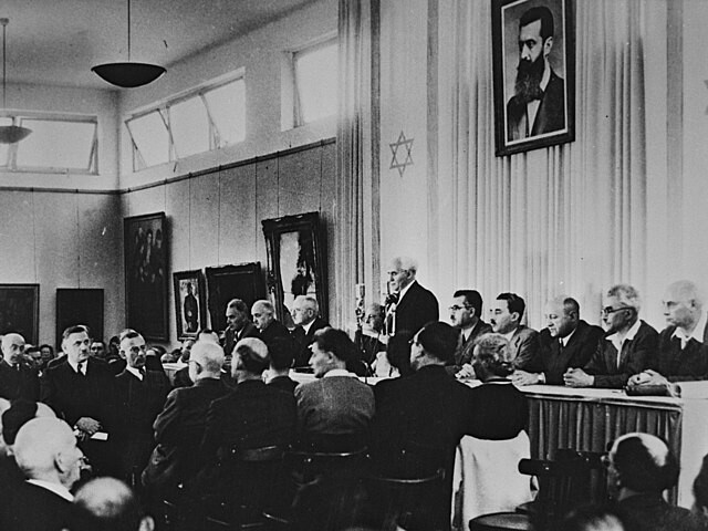 1948년 5월14일 텔아비브 박물관에서 다비드 벤 구리온(가운데)이 이스라엘의 독립을 선언하고 있다. 그는 이스라엘의 초대 총리가 된다. 대형 액자 속 인물은 현대 시오니즘의 창시자 테오도어 헤르츨. 위키미디어 코먼스