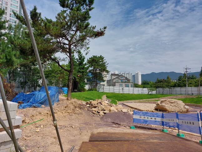 입구 차단막에 난 구멍으로 살펴본 유적 모습. 고인돌 상석 왼쪽 둔덕에 푸른 포장을 치고 쌓은 것이 무단으로 들어낸 뒤 아직 심지 않은 묘역 박석들의 무더기다.