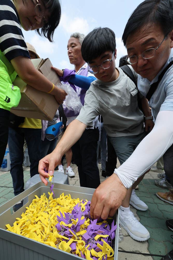 10·29 이태원참사 진상규명 특별법 제정 촉구를 위한 집중공동행동의 날 행진 참가자들이 ‘진실의 보라리본’과 ‘세월호 노란리본’이 함께 담긴 함에서 리본을 꺼내고 있다. 김정효 기자