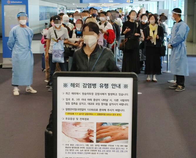 27일 오전 인천국제공항 제1터미널 입국장에 독일 프랑크푸르트와 우즈베키스탄발 탑승객들이 검역을 받기 위해 대기하고 있다. 승객들 앞에는 원숭이두창 관련 안내문이 세워져 있다. 연합뉴스