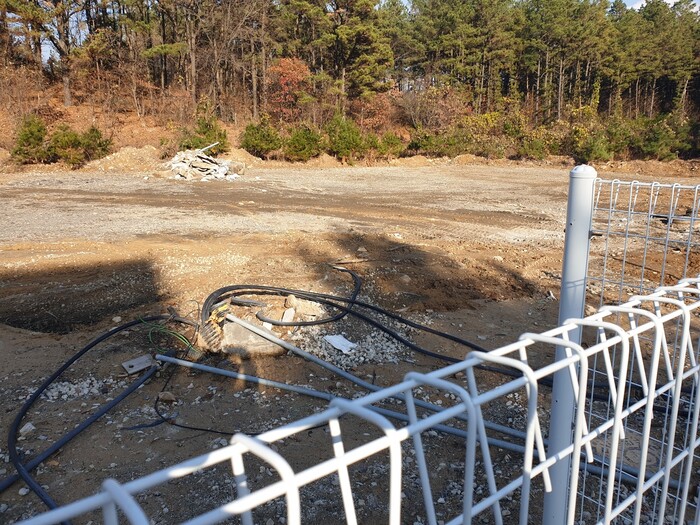 지난 25일 오후 학교 쪽과 사유지 경계지점에 철제울타리가 설치돼 있고, 사유지 땅에는 전선과 배관 등이 널브러져 있다. 박임근 기자