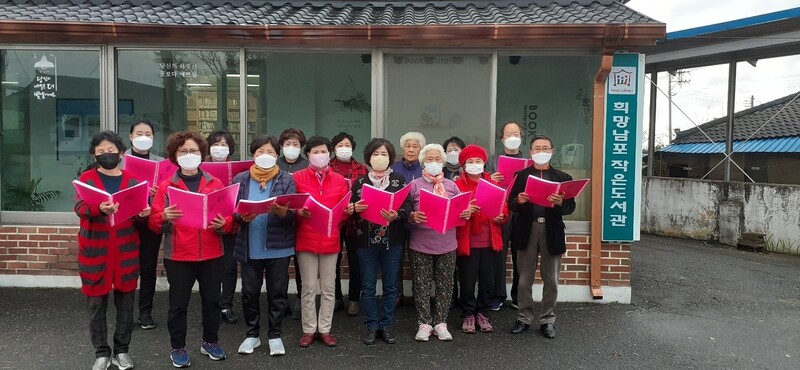 독서를 권장하고 자긍심을 갖도록 하기 위해 도서관 찬가를 만든 전북 김제 희망남포 작은도서관. 도서관 앞에서 주민들이 악보가 든 파일을 들고 사진을 찍었다. 남포도서관 제공