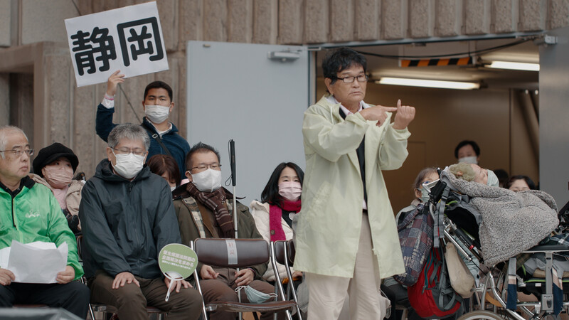 2022년 12월25일 일본 도쿄에서 옛 우생보호법 문제의 전면 해결을 목표로 하는 전국 집회에 참가한 시즈오카현 대리인이 80대 농인 여성의 사례를 전하는 모습. 영화사 고래 제공
