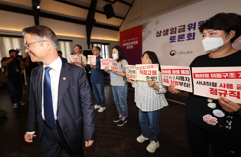 이정식 고용노동부 장관(왼쪽)이 23일 오후 서울 중구 정동1928아트센터에서 열린 상생임금위원회 토론회에 참석한 가운데 비정규직이제그만 활동가들이 비정규직 임금 대폭 인상, 노동시장 이중구조 해결 등을 촉구하는 손팻말을 들고 기습시위를 벌였다. 연합뉴스.