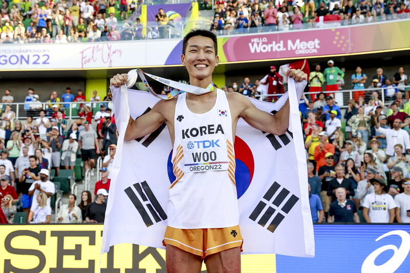 우상혁이 19일(한국시각) 미국 오리건주 유진 헤이워드필드에서 열린 2022 세계육상선수권대회 남자 높이뛰기 결선에서 은메달을 차지한 뒤 메달과 태극기를 들어 보이며 환하게 웃고 있다. 유진/EPA 연합뉴스