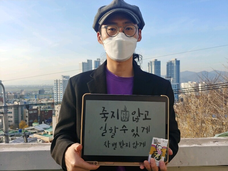 허태준 작가가 태안화력발전소 사고로 숨진 김용균 2주기를 추모하며 “죽지 않고 일할 수 있게, 차별받지 않게”라고 적힌 팻말을 들고 있다. 허태준 제공.