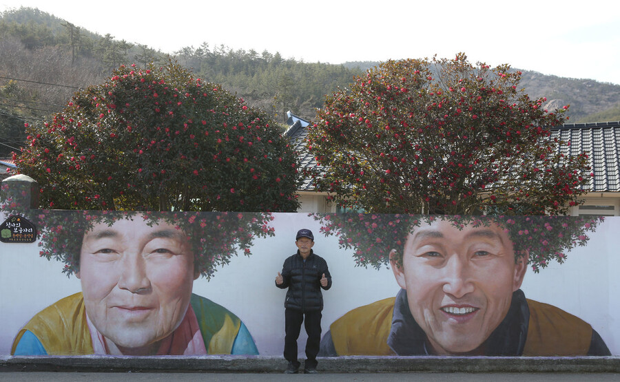 지난달 4일 신안군 암태도 기동삼거리 ‘동백 파마머리’ 벽화 앞에 선 벽화 주인공이자 집주인 문병일씨. 김선식 기자