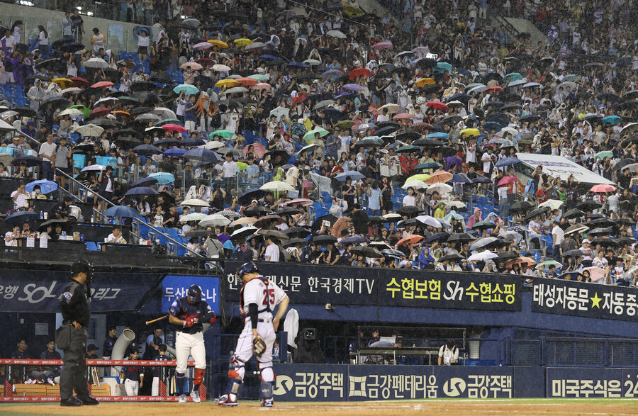 25일 서울 잠실야구장에서 열린 2023 KBO리그 두산 베어스와 롯데 자이언츠의 경기 7회초 갑자기 비가 내리자 관객들이 우산을 쓰고 응원을 이어가고 있다. 연합뉴스