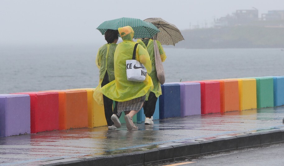 제주도가 장마철에 접어든 25일 제주시 도두동 무지개 해안도로에서 관광객들이 비옷을 입고 우산을 쓴 채 길을 걷고 있다. 연합뉴스