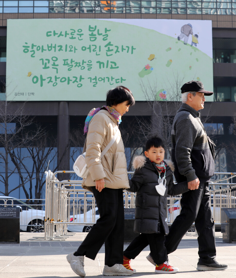 광화문 교보생명빌딩에 걸려있는 광화문글판 봄편 앞으로 27일 오전 한 어린이가 할아버지, 할머니의 손을 잡고 걷고 있다. 김혜윤 기자