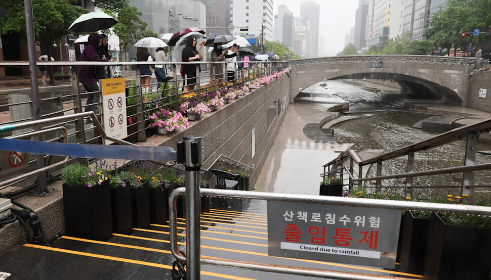 전국 대부분 지역에 비가 내린 28일 오전 우산을 쓴 외국인 관광객들이 침수 위험으로 출입이 통제된 서울 청계천 산책로 옆으로 지나가고 있다. 김정효 기자