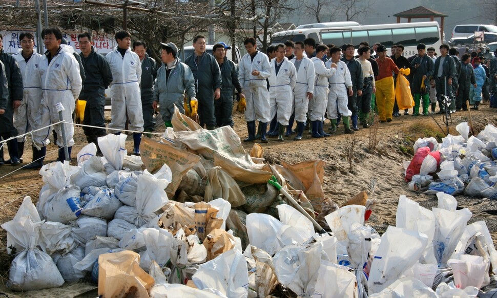 태안기름유출사고가 발생한지 일주일이 지난 2007년 12월14일 충남 태안군 모항에서 자원봉사자들이 줄지어 현장 투입을 기다리고 있다. 앞에 전날 걷어낸 원유에 젖은 모래포대가 쌓여 있다. 송인걸 기자