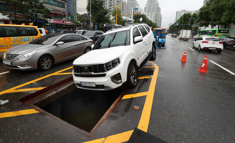 전날 내린 폭우로 불어난 물에 갇혔던 시민들이 두고 대피한 차량이 9일 오전 서울 강남구 은마아파트 앞 남부순환로 위에 위태롭게 놓여 있다. 차량 아래로 아스팔트 지하 덮개가 열려있다. 김정효 기자