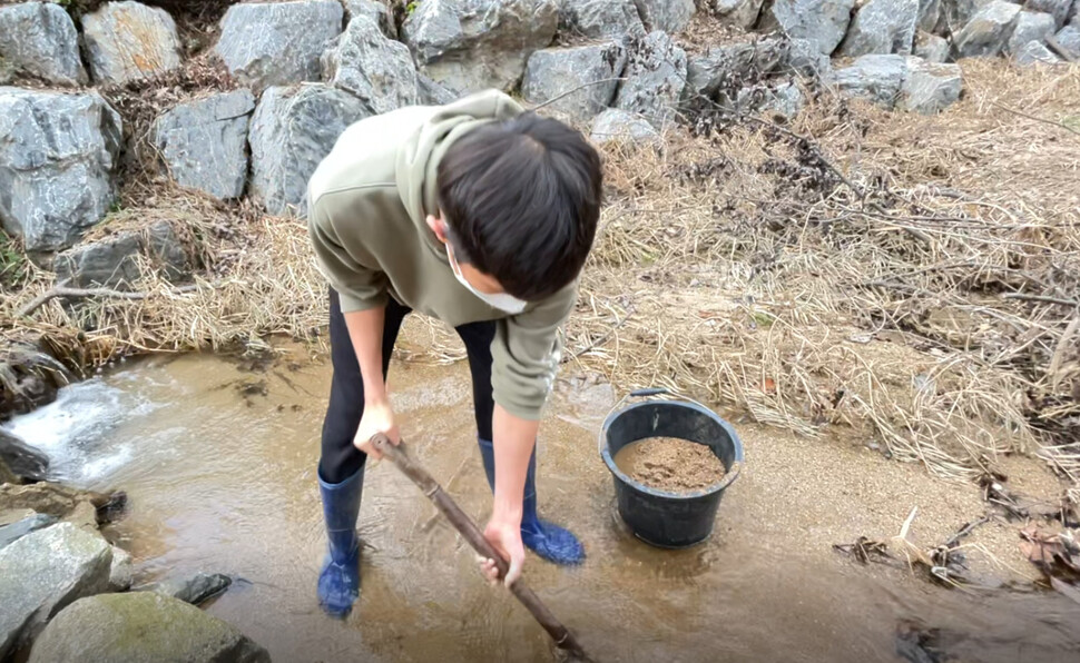 한 학생이 계곡에서 물장군 사육장에 깔 모래와 물을 채취하고 있다.