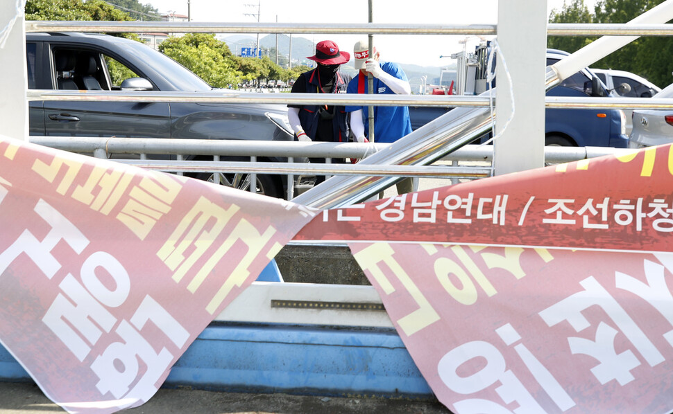 20일 오전 경남 거제 대우조선해양 옥포조선소 서문 앞에 걸려있다 훼손된 펼침막 건너에서 금속노조 경남지부 거제·통영·고성 조선하청지회 조합원들이 깃발을 건 대나무 대를 세우고 있다. 김혜윤 기자