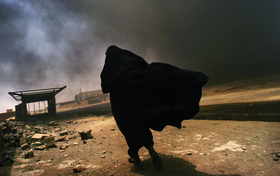 후세인 정권이 무너진 후 폐허가 된 시가지를 걷고 있는 이라크 여성. 2003년. 사진 린지 아다리오, 문학동네 제공.