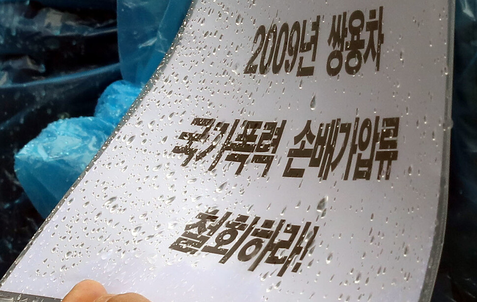 쌍용차 국가손해배상 및 국가폭력 피해 당사자들이 30일 오전 서울 서대문구 경찰청 앞에서 연 경찰의 손해배상 소송 취하 촉구 기자회견에서 한 참석자가 빗방울이 맺힌 손팻말을 든 채 노동자들의 발언을 듣고 있다. 윤운식 선임기자