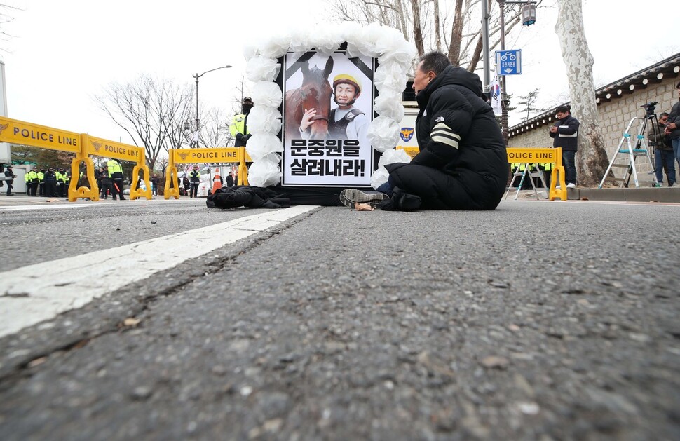 마사회 고 문중원 기수 죽음의 진상규명과 책임자 처벌을 위한 시민대책위원회 위원들과 유가족들이 6일 오전 서울 종로구 광화문소공원 추모분향소를 출발해 청와대로 헛상여를 들고 행진하다 경찰에 가로막혀 서 있다. 문 기수의 아버지 문군옥씨가 아들의 사진을 바라보며 눈물 흘리고 있다. 백소아 기자