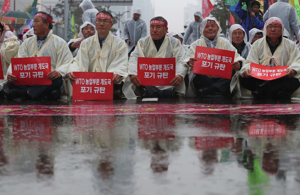 13일 오후 서울 여의도 국회 앞에서 열린 한국농업경영인중앙연합회 주최 전국농민총궐기 대회에서 빗물에 젖은 아스팔트 위로 거리에 앉은 참가자들의 모습이 비치고 있다. 박종식 기자