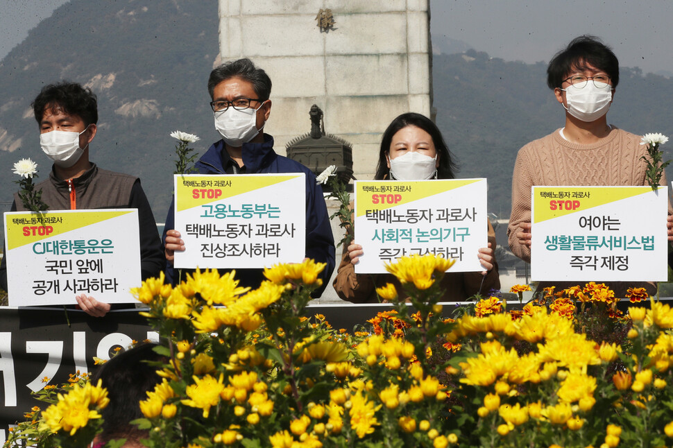 지난 19일 오후 서울 광화문광장 이순신 동상 앞에서 열린 ‘대기업 택배사 규탄과 택배노동자 과로사 예방 호소하는 택배 소비자 기자회견’에서 참석자들이 추모 국화와 손팻말을 들고 있다. 연합뉴스