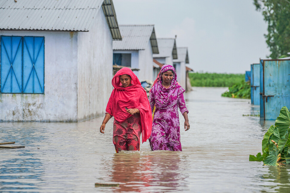 방글라데시 보구라에서 여성들이 홍수로 잠긴 도로에서 전통의상인 사리를 입고 어렵게 물살을 헤쳐나가고 있다. 카본 브리프 제공