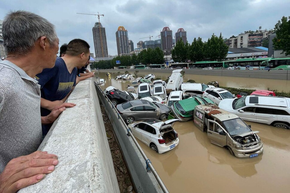 21일 중국 정저우 시민들이 폭우로 강변에 주차된 차량이 떠내려와 쌓여있는 모습을 지켜보고 있다. 정저우/AFP 연합뉴스
