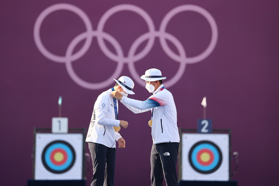 김제덕 선수(오른쪽)가 코로나19 거리두기로 안산 선수에게 금메달을 걸어주고 있다. 도쿄/연합뉴스