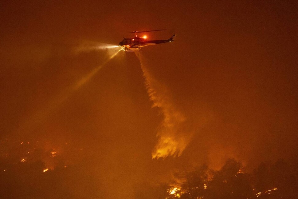 한 소방헬기가 지난달 24일(현지시각) 미국 캘리포니아 프렌치 파이어에서 산불이 주택가를 덮치려 하자 공중에서 물을 뿌리고 있다. 연합뉴스