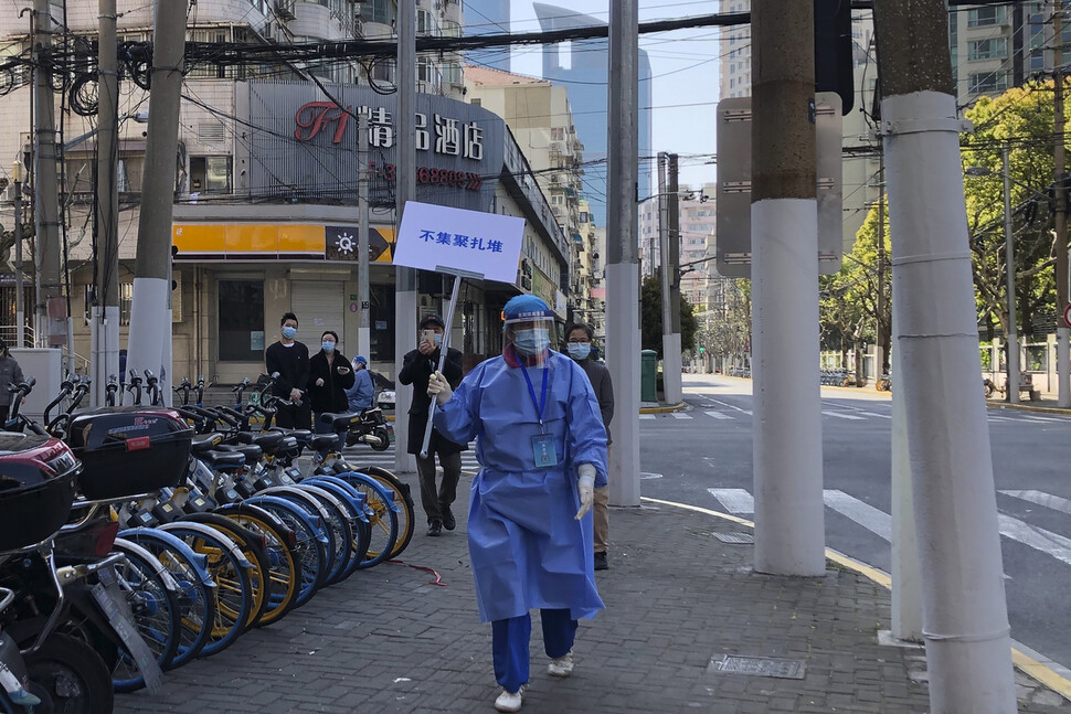 코로나19 전수 검사가 진행 중인 지난 4일 중국 상하이 서부 징안지구의 봉쇄 지역에서 보호복을 착용한 사람이 전염을 막기 위한 거리 두기 캠페인 문구가 적힌 손팻말을 들고 거리를 걸어가고 있다. 중국 당국은 군 인력 2천 명을 포함해 전국에서 차출한 의료 인력 1만 명 이상을 상하이로 파견해 코로나19 검사를 지원토록 했다. 상하이/AP 연합뉴스