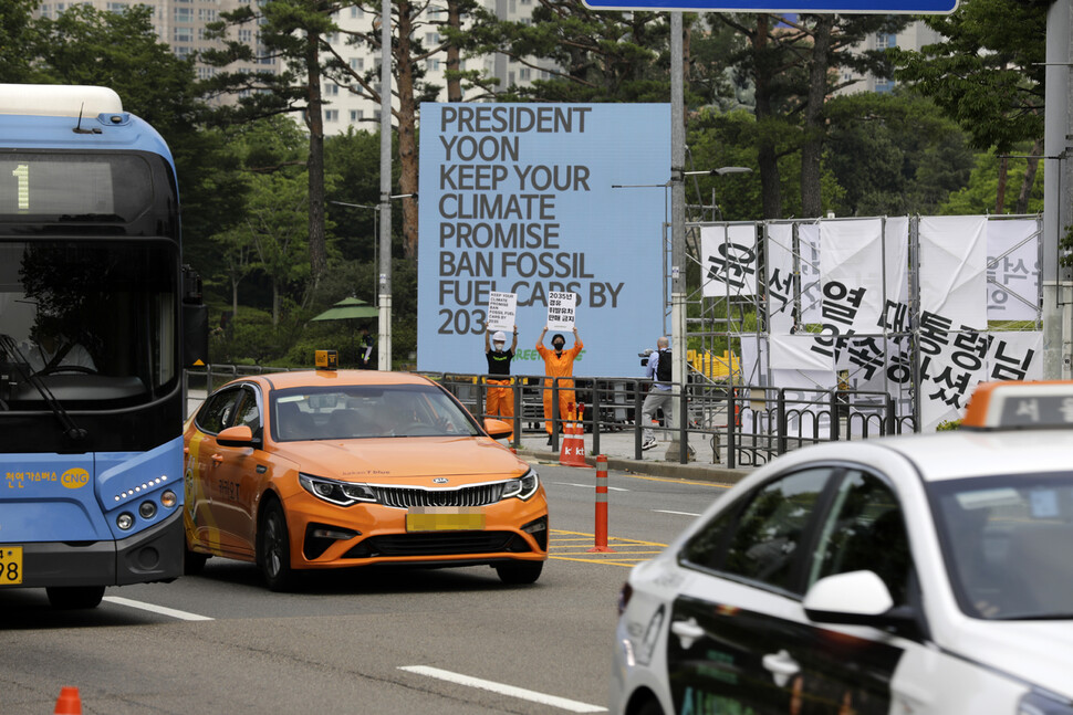 그린피스 활동가들이 5일 오전 서울 용산 대통령실 앞에서 ‘2035년 탈내연기관’ 약속이행 촉구하는 손팻말을 들고 있다. 가로 4.5m, 세로 4.5m 전광판으로 이뤄진 비디오 아트 작품에는 ‘윤석열 대통령님, 기후공약을 지키세요. 2035년 내 내연기관차 판매 금지’라는 문구가 나오고 있다. 김명진 기자