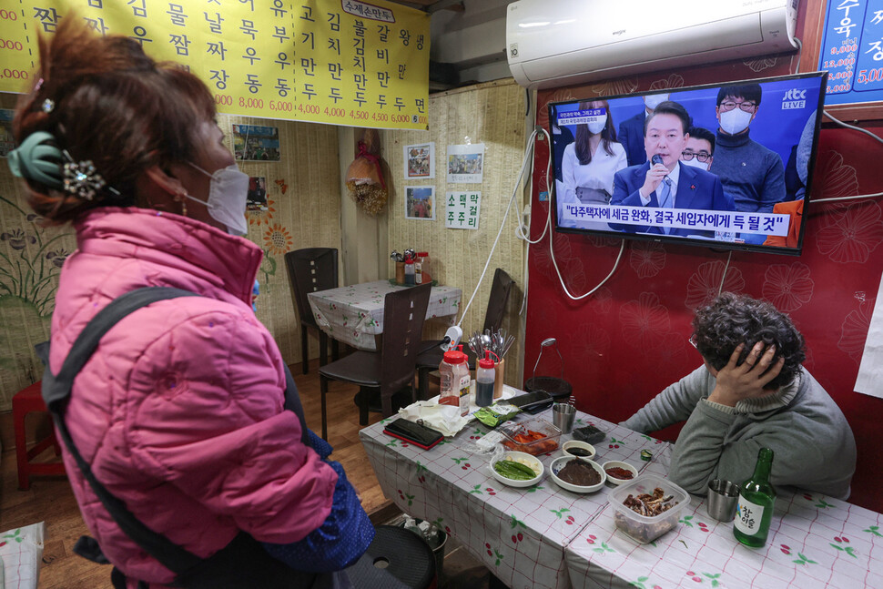 윤석열 대통령 주재로 제1차 국정과제점검회의가 열린 지난 15일 오후 서울 마포구 망원시장에서 한 상인이 중계방송으로 회의를 시청하고 있다. ‘다주택자에 세금 완화, 결국 세입자에게 득 될 것’이라고 쓰인 자막이 보인다. 연합뉴스