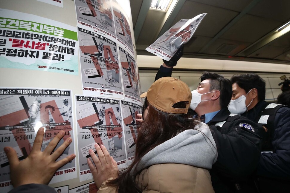 전국장애인차별철폐연대 활동가들이 홍보물을 역사 안에 있는 기둥에 붙이자 서울교통공사 직원들이 떼어내고 있다. 김혜윤 기자