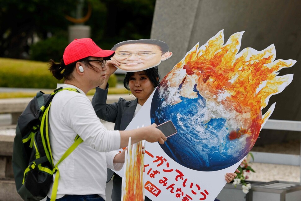 18일 주요 7개국(G7) 정상회의 반대 시위에 참가한 두 명의 활동가가 팻말과 마스크를 들고 있다. AFP 연합뉴스