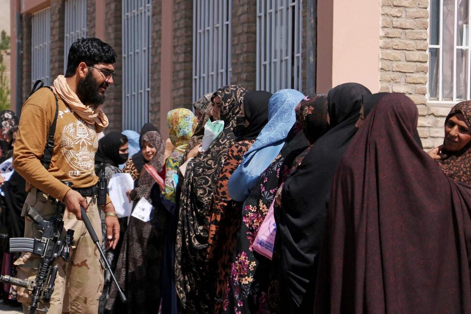 26일 아프가니스탄 헤랏에서 탈레반 보안요원 한 명이 공공기관 앞에서 길게 줄을 서 있는 여성들을 단속하고 있다. AFP 연합뉴스