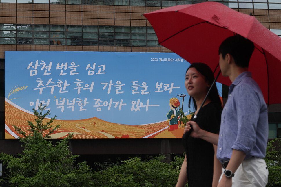 교보생명 홍보 담당 직원들이 광화문글판 가을편 앞으로 우산을 쓰고 지나가고 있다. 김혜윤 기자