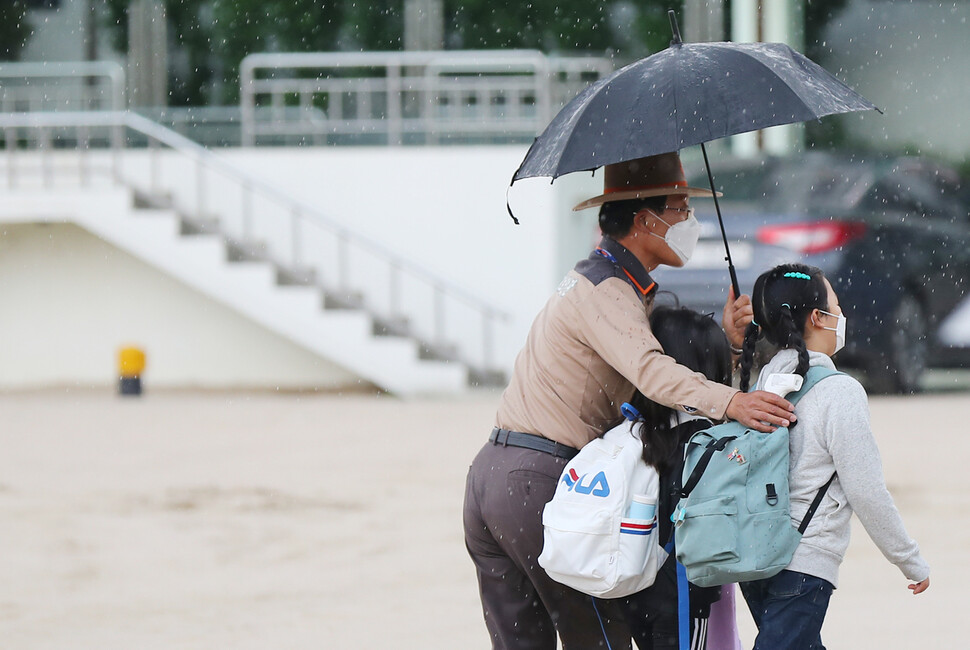 소나기가 내린 지난 5월28일 오전 서울 종로구 한 초등학교에서 학교보안관이 우산을 미처 준비하지 못한 아이들에게 우산을 씌워주며 교실로 함께 이동하고 있다. 연합뉴스