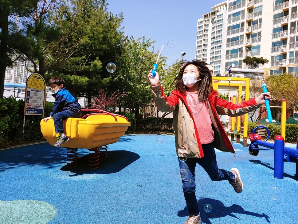 초등학교 4학년 김세빈 양(오른쪽)이 한산한 놀이터에서 마스크를 쓴 채 비눗방울을 만들고 있다. 김 양의 아버지는 학교 가지 않는 아이들을 돌보는 동안 긴급재난지원금으로 인한 여유가 단비와 같았다고 말한다.