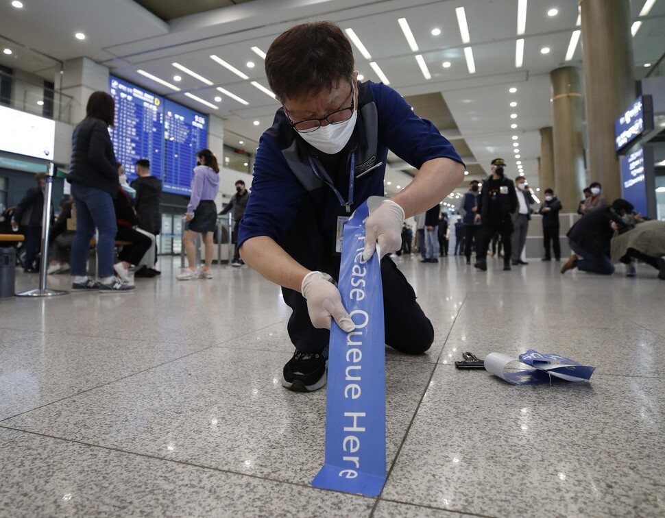 인천국제공항 제1터미널 입국장에 해외입국자에게 특별수송교통수단을 타기 위해 줄 서 달라는 문구가 적힌 화살표 테이프를 한 직원이 바닥에서 떼어내고 있다. 인천공항/김혜윤 기자