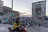 19일(현지시각) 튀르키예 하타이주 한 유치원 지진 피해 현장 앞으로 오토바이를 탄 구급대원이 지나가고 있다. 그 뒤로 유치원 건물 잔해에 이번 지진으로 숨진 어린이들을 추모하는 풍선이 묶여 있다. 하타이/로이터 연합뉴스