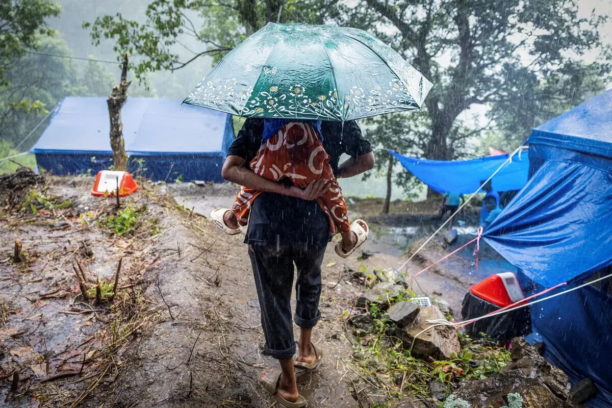A person carries a child under an umbrella near makeshift shelters at a temporary camp in Nepal on Sept. 9, 2026, following severe monsoon floods and landslides. (Retuers/Yonhap)