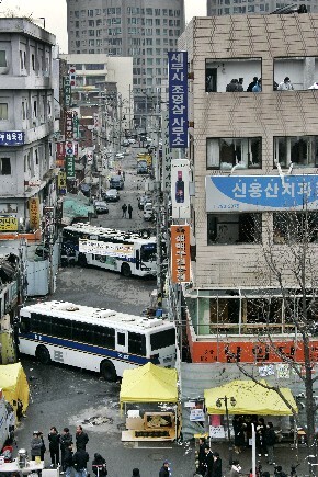  police buses block the roads around the building where a civilian demonstration two days earlier against a redevelopment project resulted in the deaths of five civilians and one police officer. The 5-story building where the deadly incident took place is on the right.