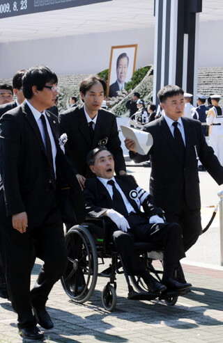 8월23일 서울 여의도 국회에서 진행된 김대중 전 대통령 영결식에서 진행요원들이 헌화·분향을 마친 장남 김홍일 전 의원(휠체어에 탄 이)을 뜨거운 햇볕을 피해 그늘로 옮기고 있다. 사진공동취재단