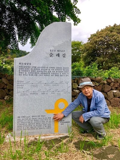 Jeong at a stone marker honoring Taquet during his pilgrimage in front of Jeju Island’s only rice farm. (provided by Da Vinci)