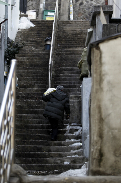 An elderly man carries winter relief supplies he received from the Korea Red Cross up a staircase in Seoul’s Yongsan district.
